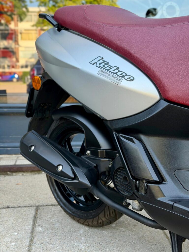 Close-up van de achterzijde van een scooter met rood zadel en zwarte uitlaat.