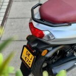 Achterkant van een zilvergrijze scooter met bordeauxrood zadel, achterlicht en kenteken.