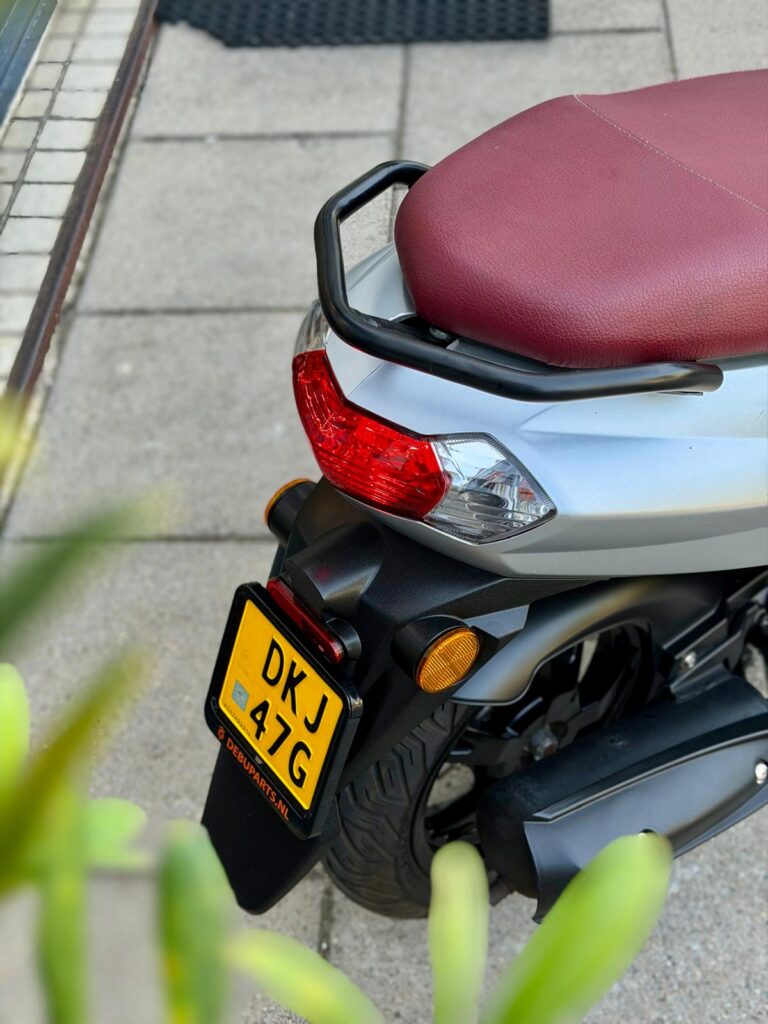 Achterkant van een zilvergrijze scooter met bordeauxrood zadel, achterlicht en kenteken.