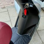 Close-up van een scooter met rood zadel, contactsleutel met rood label in het contactslot.