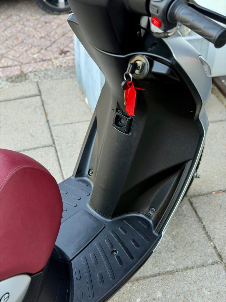 Close-up van een scooter met rood zadel, contactsleutel met rood label in het contactslot.