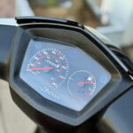 Close-up van scooterdashboard met snelheidsmeter en brandstofmeter, zwarte behuizing.