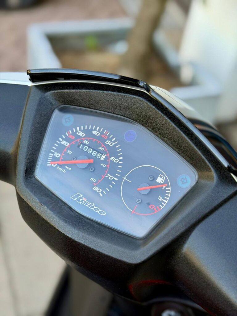 Close-up van scooterdashboard met snelheidsmeter en brandstofmeter, zwarte behuizing.