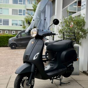 Matzwarte scooter met hoog windscherm op standaard, geparkeerd voor een showroom.