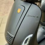 Detail van de voorkap van een matte grijze scooter met koplamp, LED-knipperlicht en Sourini R-embleem.