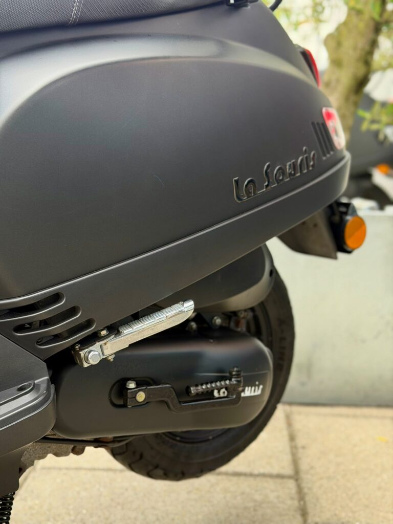 Close-up van de matte zwarte scooter, met voetsteun, wiel en La Souris-logo.