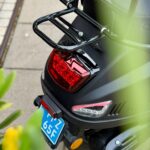 Close-up van de achterkant van een zwarte scooter met bagagedrager, remlicht en blauwe kentekenplaat.