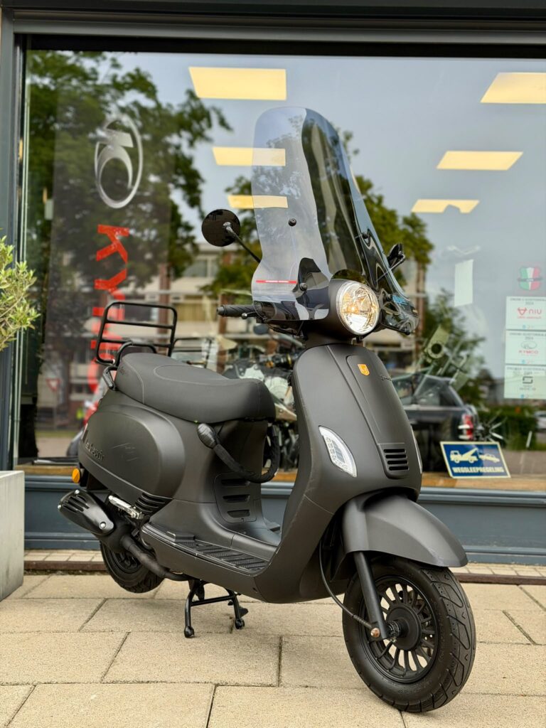 Mat zwarte scooter met hoog windscherm op standaard, geparkeerd voor een scooterwinkel