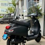 Zwarte La Souris scooter met windscherm geparkeerd voor een werkplaats of showroom.