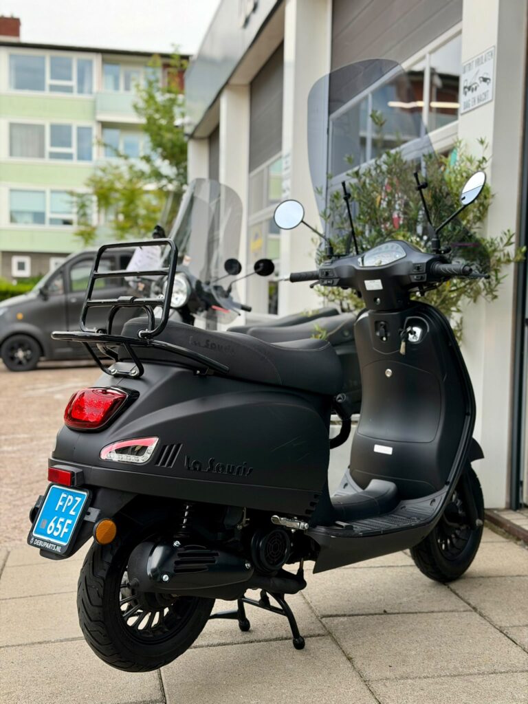 Zwarte La Souris scooter met windscherm geparkeerd voor een werkplaats of showroom.