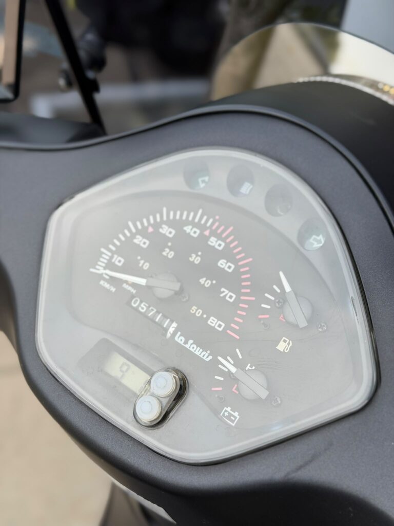 Close-up van het dashboard van een scooter met snelheidsmeter, brandstof- en temperatuurmeter.