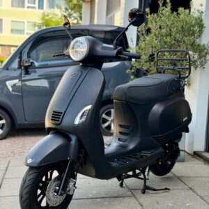 Mat zwarte scooter op standaard voor een garage, met stadsauto op de achtergrond.