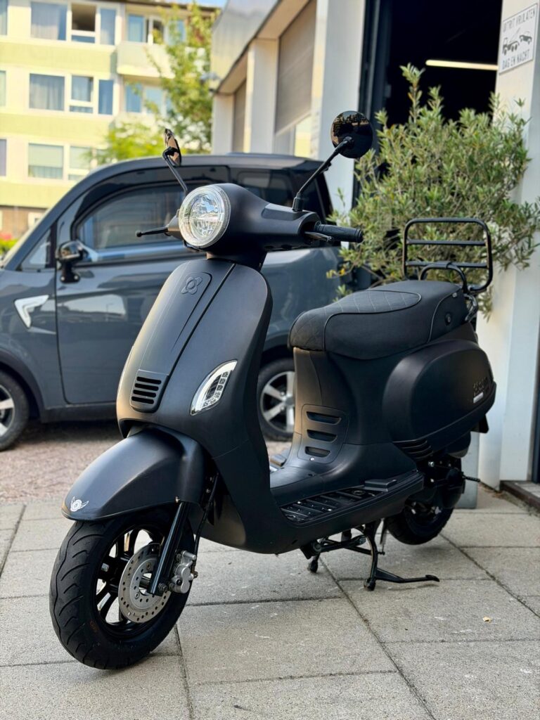 Mat zwarte scooter op standaard voor een garage, met stadsauto op de achtergrond.