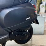 Detail van zwarte AGM-scooter met achterwiel, motor en zadel zichtbaar, buiten op stoep geparkeerd.