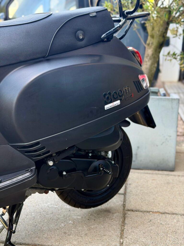 Detail van zwarte AGM-scooter met achterwiel, motor en zadel zichtbaar, buiten op stoep geparkeerd.