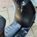 Close-up van een zwarte scooter met sleutels in het contact en de treeplank op straat.
