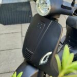 Close-up van de voorkant van een matte zwarte scooter met ronde koplamp en richtingaanwijzers.