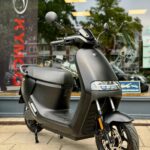 Matzwarte scooter op standaard met LED-koplamp en schijfrem, voor een winkelruit.