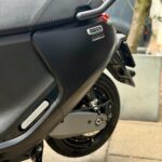 Close-up van de achterkant van een zwarte elektrische scooter met zadel, bagagedrager en achterwiel.