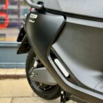 Close-up van de zijkant van een matzwarte scooter op de standaard, met zadel, handgreep en achterwiel.