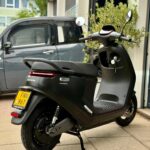 Zwarte Segway elektrische scooter op zijstandaard met gele kentekenplaat, geparkeerd bij een garage.