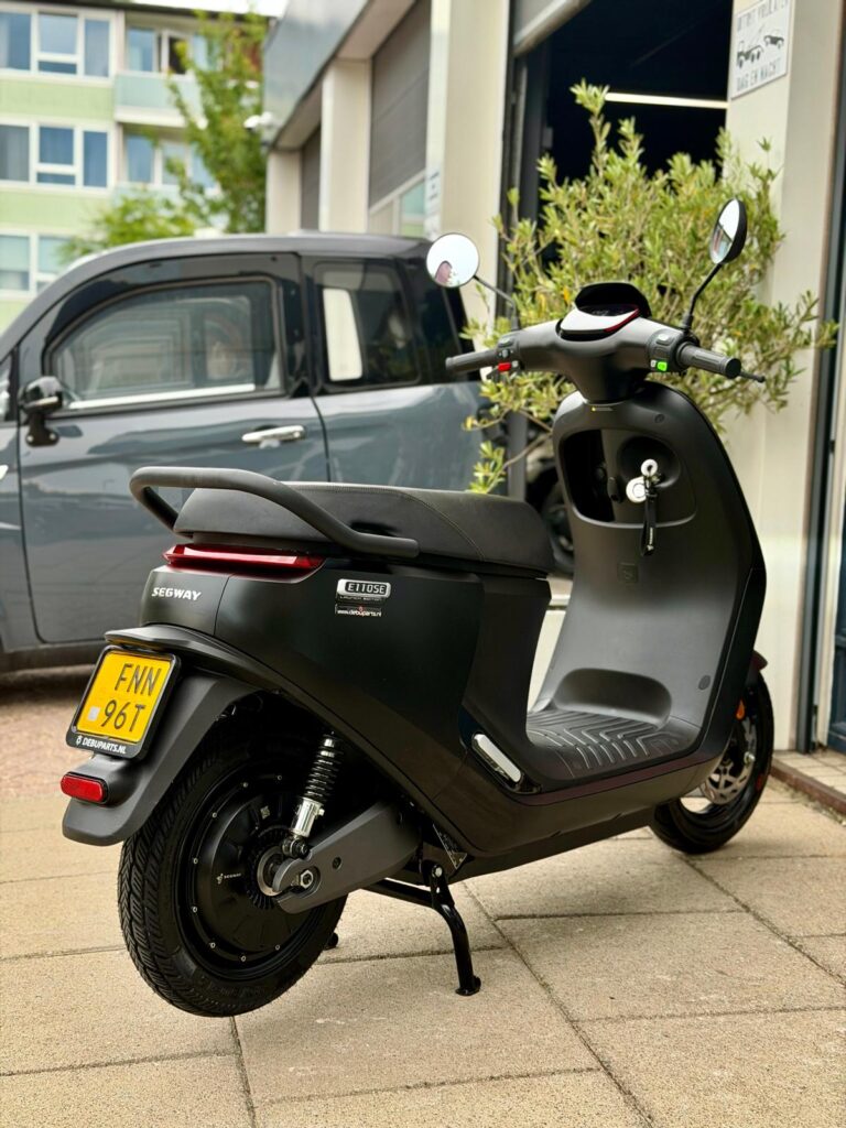 Zwarte Segway elektrische scooter op zijstandaard met gele kentekenplaat, geparkeerd bij een garage.
