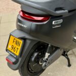 Achterzijde van een zwarte Segway E110SE elektrische scooter met geel kenteken en rood achterlicht op de stoep.