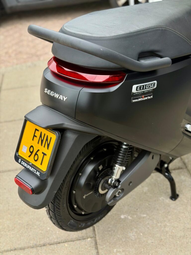 Achterzijde van een zwarte Segway E110SE elektrische scooter met geel kenteken en rood achterlicht op de stoep.