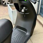 Close-up van een zwarte elektrische scooter met sleutel in het contact en rubberen voetplaat.