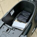 Open opbergruimte onder een scooterzadel met Segway-doosje en kabels.