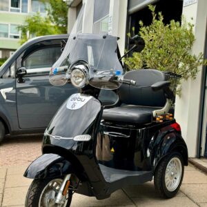 Zwarte driewielige scootmobiel met hoog windscherm, geparkeerd voor een garage.