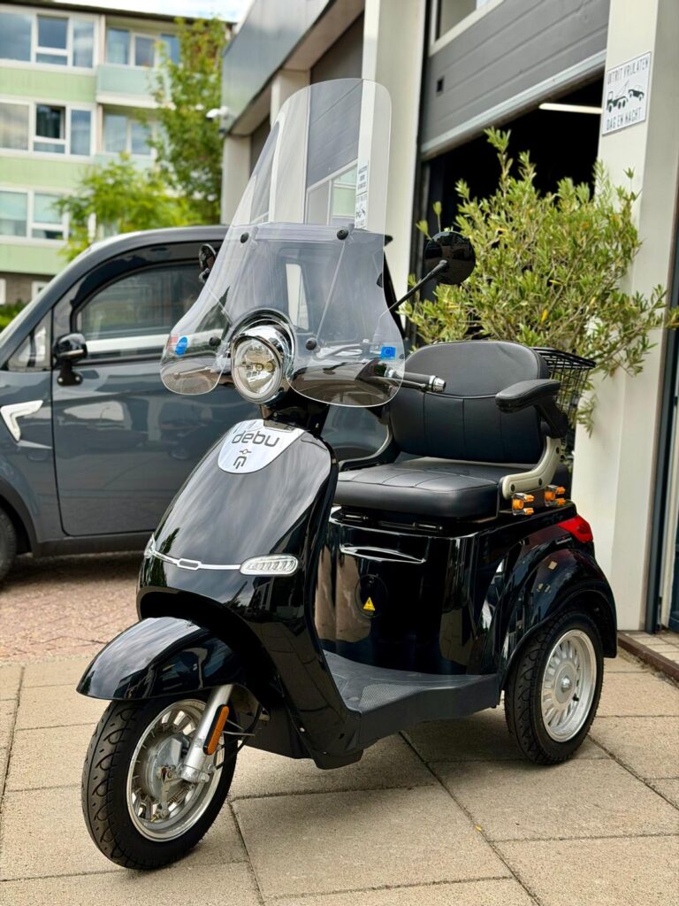 Zwarte driewielige scootmobiel met hoog windscherm, geparkeerd voor een garage.