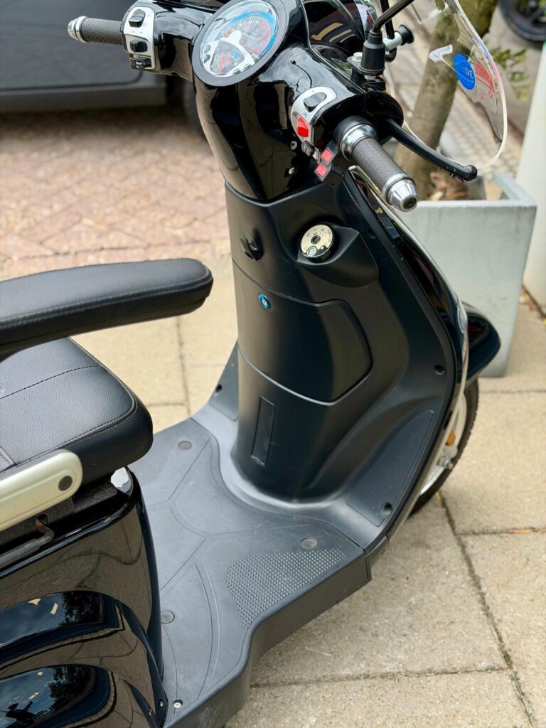 Close-up van het stuur, dashboard en voetplaat van een zwarte scooter op straat.
