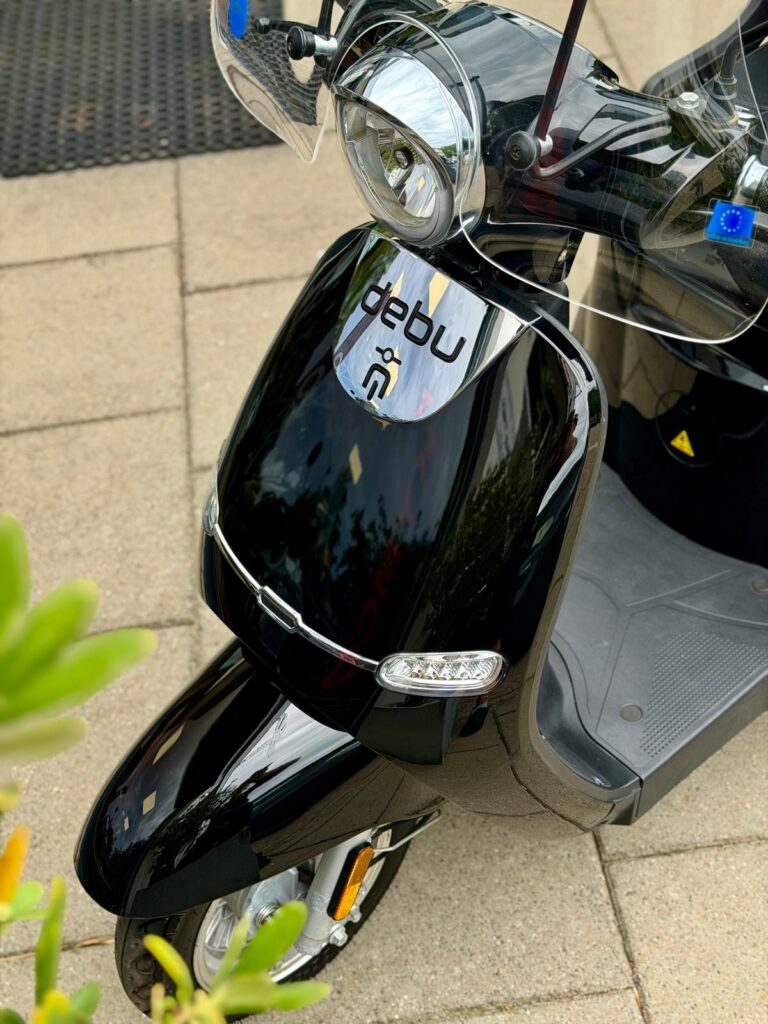 Close-up van een glanzende zwarte elektrische scooter met windscherm en ledknipperlichten