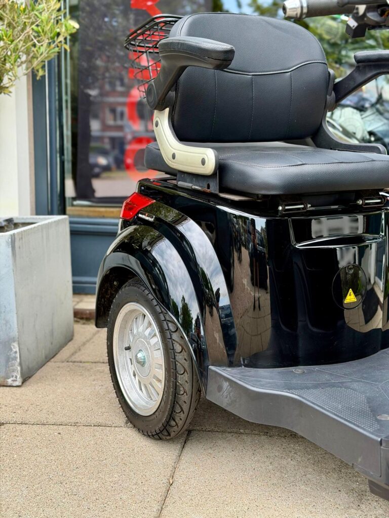 Close-up van de achterzijde van een zwarte scootmobiel met zitting, armleuningen en achterwiel op de stoep.