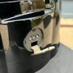 Close-up van een open ronde elektrische aansluiting met klepje in een glanzende zwarte behuizing.