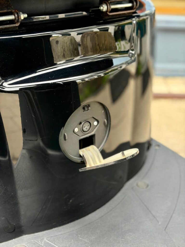 Close-up van een open ronde elektrische aansluiting met klepje in een glanzende zwarte behuizing.