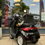 Achteraanzicht van een zwarte driewielige scootmobiel met bagagemand, geparkeerd voor een etalage.