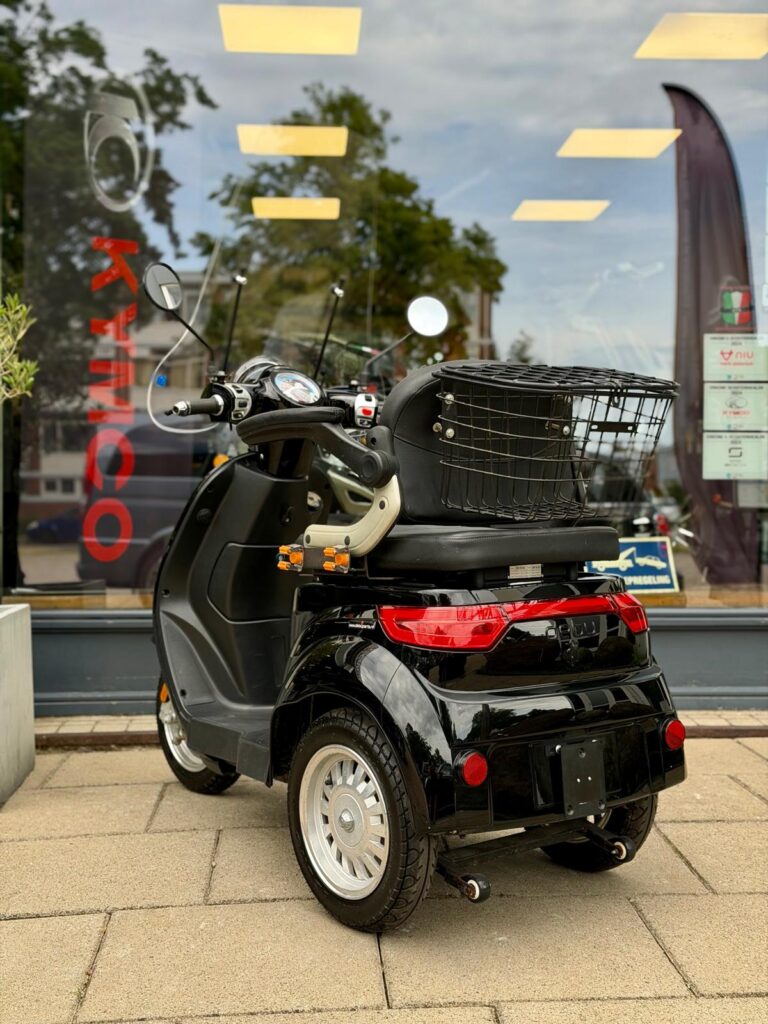 Achteraanzicht van een zwarte driewielige scootmobiel met bagagemand, geparkeerd voor een etalage.