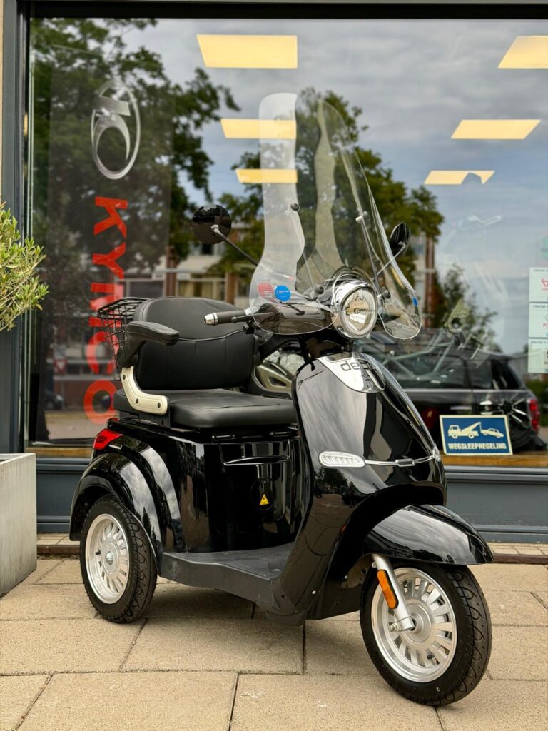 Zwarte driewielscooter met hoog windscherm, geparkeerd op de stoep voor een winkel.