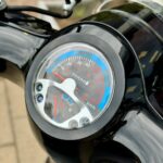 Close-up van het dashboard met snelheidsmeter en brandstofmeter van een zwarte scooter.