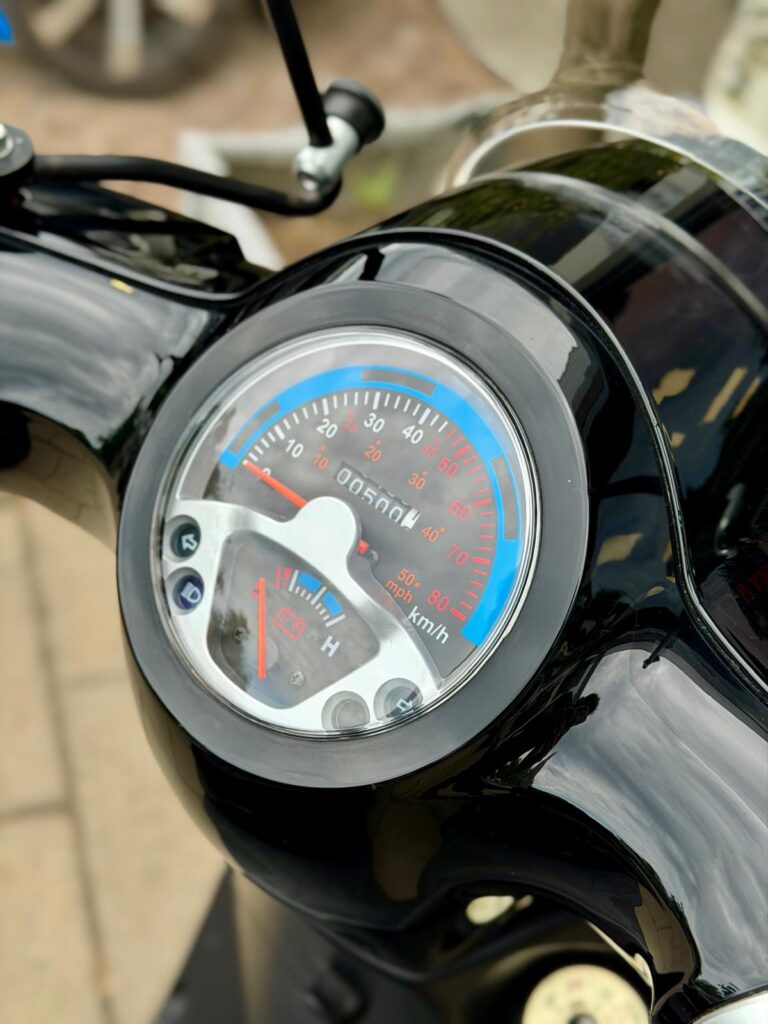 Close-up van het dashboard met snelheidsmeter en brandstofmeter van een zwarte scooter.