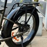 Close-up van het achterwiel van een e-bike met bagagedrager, schijfrem en brede band.
