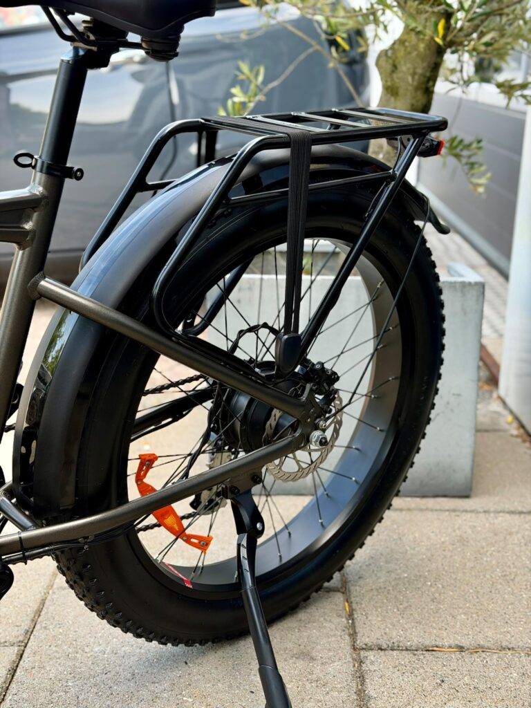 Close-up van het achterwiel van een e-bike met bagagedrager, schijfrem en brede band.