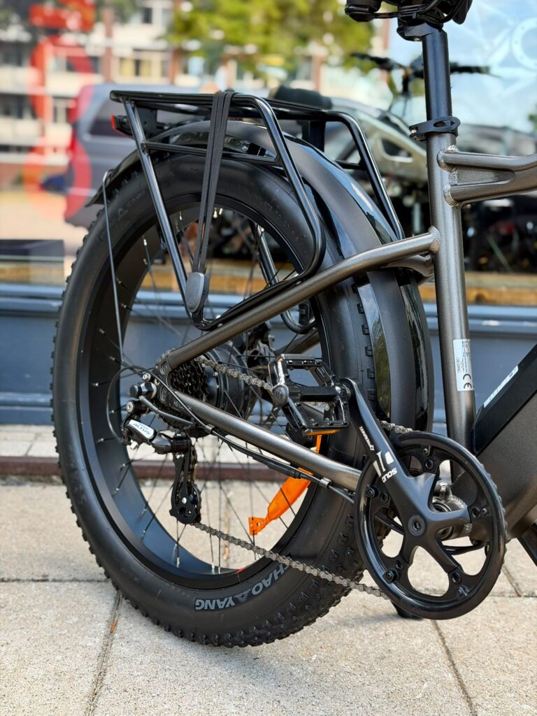 Close-up van het achterwiel en aandrijving van een fatbike e-bike met bagagedrager en spatbord.