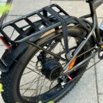 Achterzijde van een e-bike met fatbike-band, bagagedrager met snelbinders, spatbord en naafmotor.