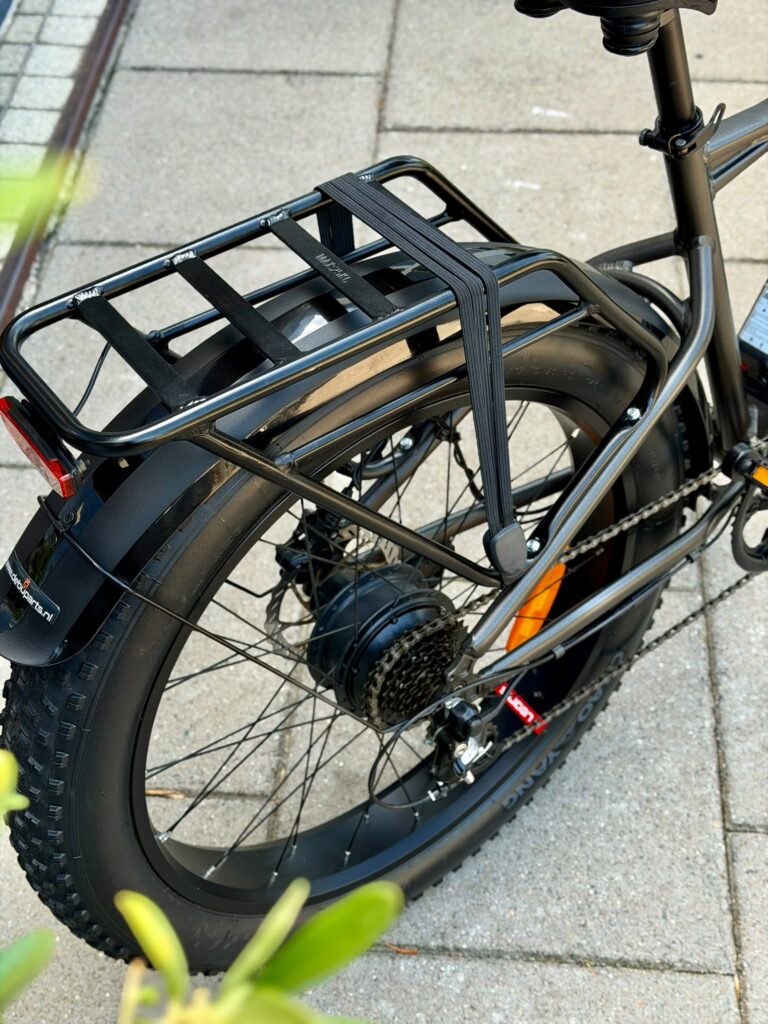 Achterzijde van een e-bike met fatbike-band, bagagedrager met snelbinders, spatbord en naafmotor.