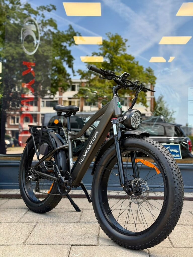 Elektrische fatbike met dikke banden, koplamp en bagagedrager, geparkeerd voor een etalage.