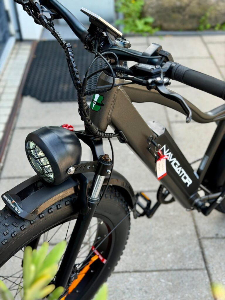 Close-up van een zwarte elektrische fatbike met dikke banden, koplamp en display op het stuur.