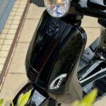 Close-up van de voorkant van een glanzende zwarte scooter met ronde koplamp en LED-dagrijlichten.